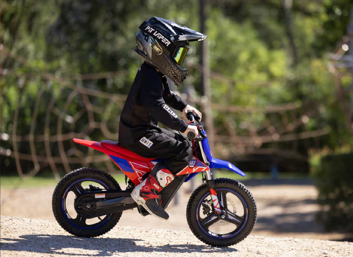 Niño con casco conduciendo una moto eléctrica RFN Warrior Kids en un camino de grava